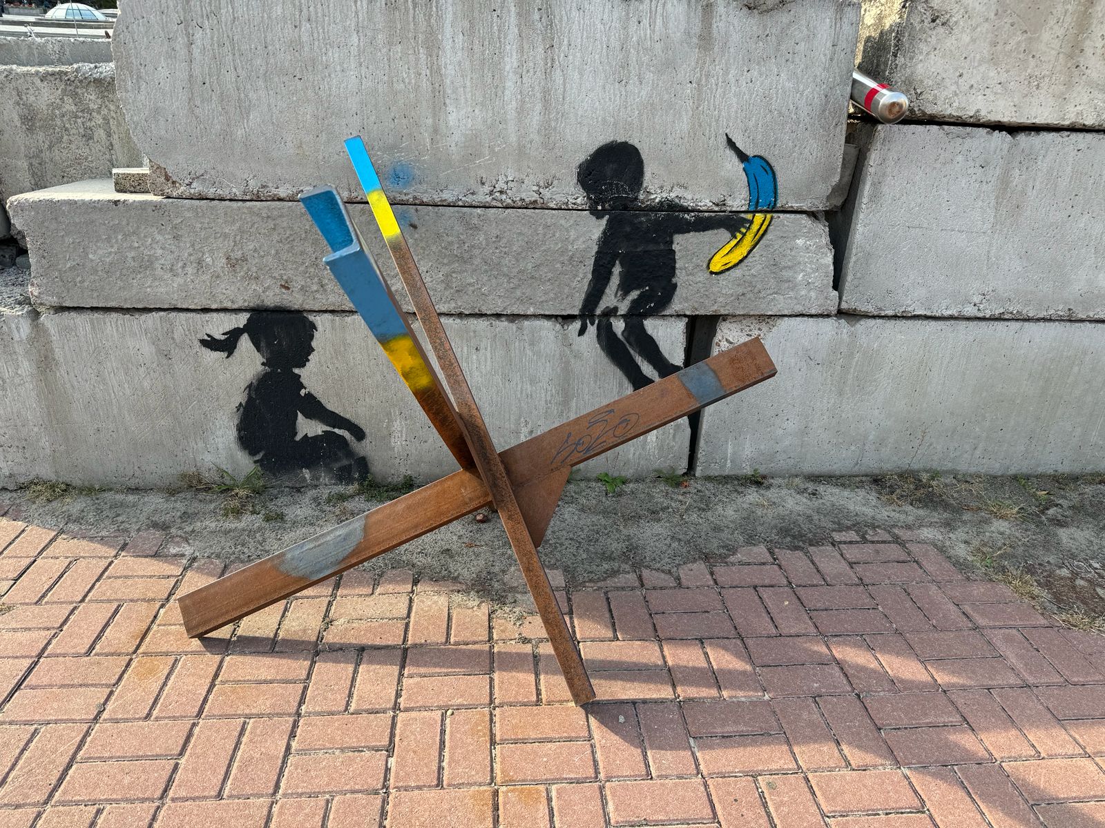 A steel anti-tank sculpture in Ukraine's colours beside stencilled street art