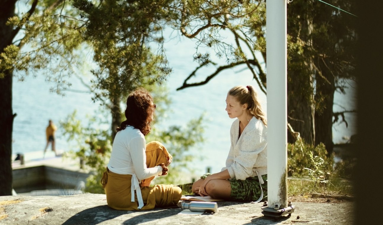 Two participants in conversation on the rocks above the water